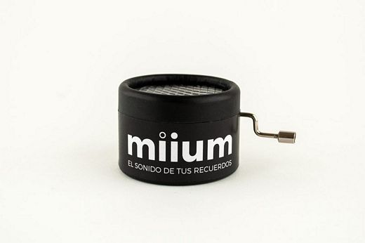 Caja redonda de color negro con el logo de miium y mecanismo de manivela. Tamaño de 5cm de diámetro y 4 de altura.